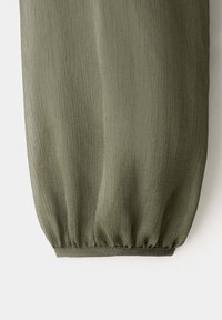Manche en tissu texturé vert olive avec poignet élastique, créant un effet froncé au niveau du poignet.