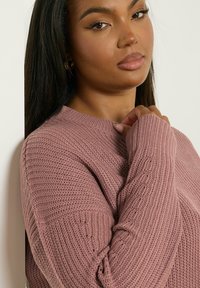 Pull en tricot rose avec une texture côtelée, col rond et manches longues. Présente une coupe ample et décontractée ainsi que des détails de couture subtils.