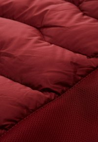 Burgundowy materiał puchowy z gładką, pikowaną teksturą z jednej strony i kontrastowym, teksturowanym wzorem siateczkowym z drugiej.