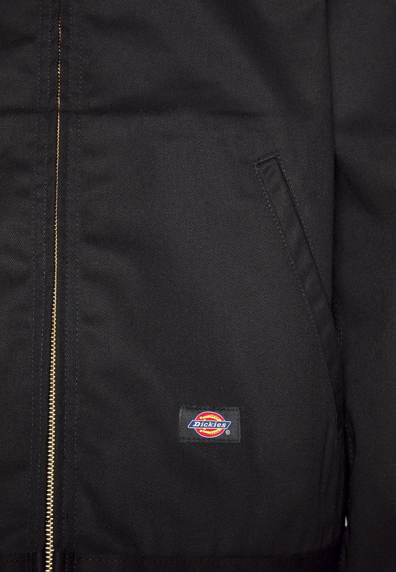 Giacca nera con zipper dorato, due tasche laterali e una toppa ricamata con il logo Dickies in basso a sinistra. Tessuto di peso consistente.