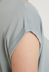 Ljusblå topp med kort ärm och rundad halsringning samt subtil plissédetalj vid axeln. Mjuk, slät tyg med avslappnad passform.