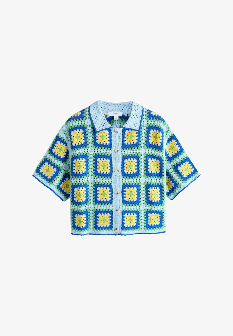 Cardigan en crochet avec un col bleu, présentant un motif carré en bleu, vert et jaune. Manches courtes, devant boutonné et tissu texturé.