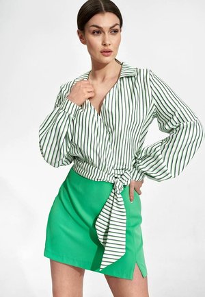 Bluzka z kołnierzykiem w stylu wrap z białymi i zielonymi pionowymi paskami oraz objętościowymi rękawami, w zestawieniu z jasnoniebieską mini spódnicą z bocznym rozcięciem.