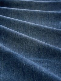 Close-up of blue denim fabric with visible weave and soft folds creating diagonal lines across the material.