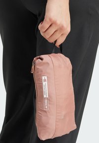 Pochette con cerniera di colore rosa chiaro, dotata di un esterno in nylon testurizzato, un manico nero per il trasporto e un'etichetta di marca bianca.