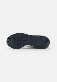 Suela de zapatilla de goma con un patrón texturizado, de color azul marino predominante, que presenta surcos de tracción elevados y un detalle de logotipo.