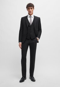 Black three-piece suit featuring a fitted blazer, waistcoat, and trousers; paired with a white shirt and patterned tie; leather shoes.