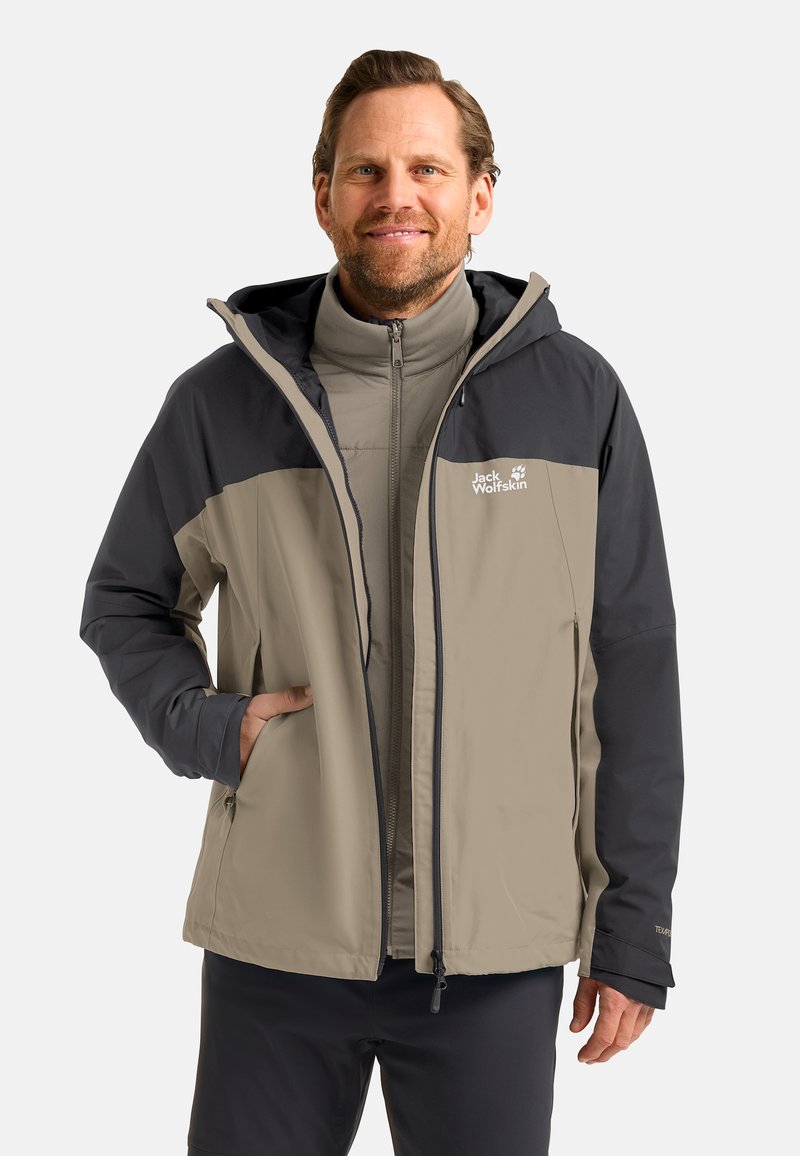 Veste imperméable en beige et marine foncé avec une fermeture éclair à l'avant, une capuche ajustable et un logo sur la poitrine. Comprend des poches latérales et des poignets élastiques.