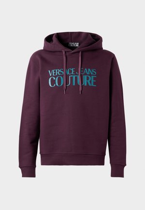 Tamno ljubičasta dukserica s kapuljačom i vezicama, s velikim tirkiznim slovima "Versace Jeans Couture" otisnutim sprijeda.