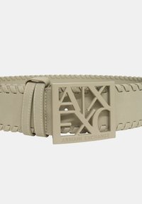 Cintura in pelle beige con texture intrecciata, dotata di una fibbia con logo intagliato che recita "ARMANI EXCHANGE" in un colore beige abbinato.