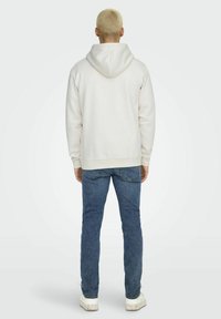 Hellgrauer Hoodie mit geräumiger Kapuze, Rippbündchen und -saum. Kombiniert mit blauen Jeans und weißen Sneakers. Glatte Textur, lässige Passform.