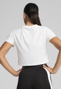 Besparet hvid t-shirt med korte ærmer og rund halsudskæring, glat tekstur, parret med højtaljede sorte leggings med hvide sideaccentuer.