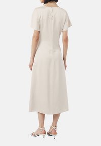 Beżowa sukienka do kolan z krótkimi rękawami, wysokim dekoltem i detalem w postaci łezki z tyłu; gładki, lekki materiał o delikatnym połysku.