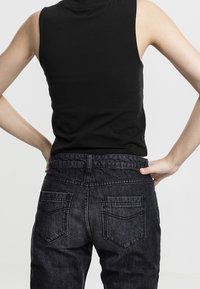 Top sans manches noir associé à un jean en denim foncé, avec une taille haute et deux poches arrière ornées d'un motif de couture subtil.