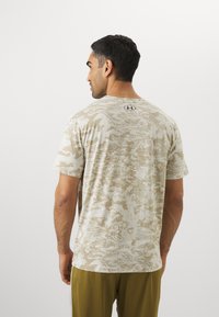 Beige camouflage t-shirt, korte ærmer, rund hals, blød tekstur, har et subtilt digitalt trykmønster, mærket logo på ryggen.