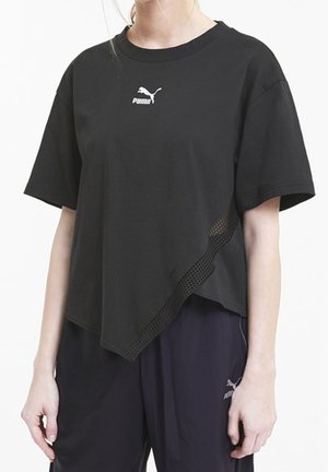 T-shirt noir Puma à manches courtes avec ourlet asymétrique et détail en mesh, porté avec un pantalon Puma foncé sur une personne debout.