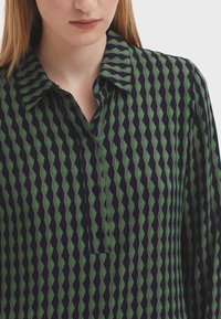 Button-up shirt with a green and navy diamond pattern, collared design, soft texture, and black buttons along the placket.