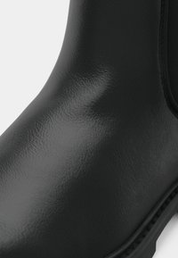 Botín negro impermeable con textura de cuero suave, forma redondeada, paneles laterales elásticos y suela de goma duradera.