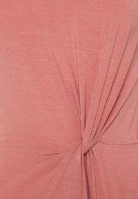 Mjuk korallfärgad tyg som samlas och vrids i mitten, vilket skapar veck och textur på ett slätt och lätt material.