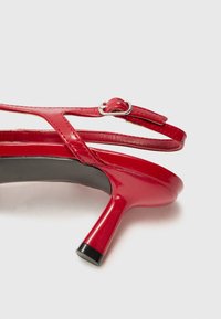 Red patent leather high heel sandal with a sleek design, adjustable ankle strap, and a gently curved heel. Black sole detail visible.