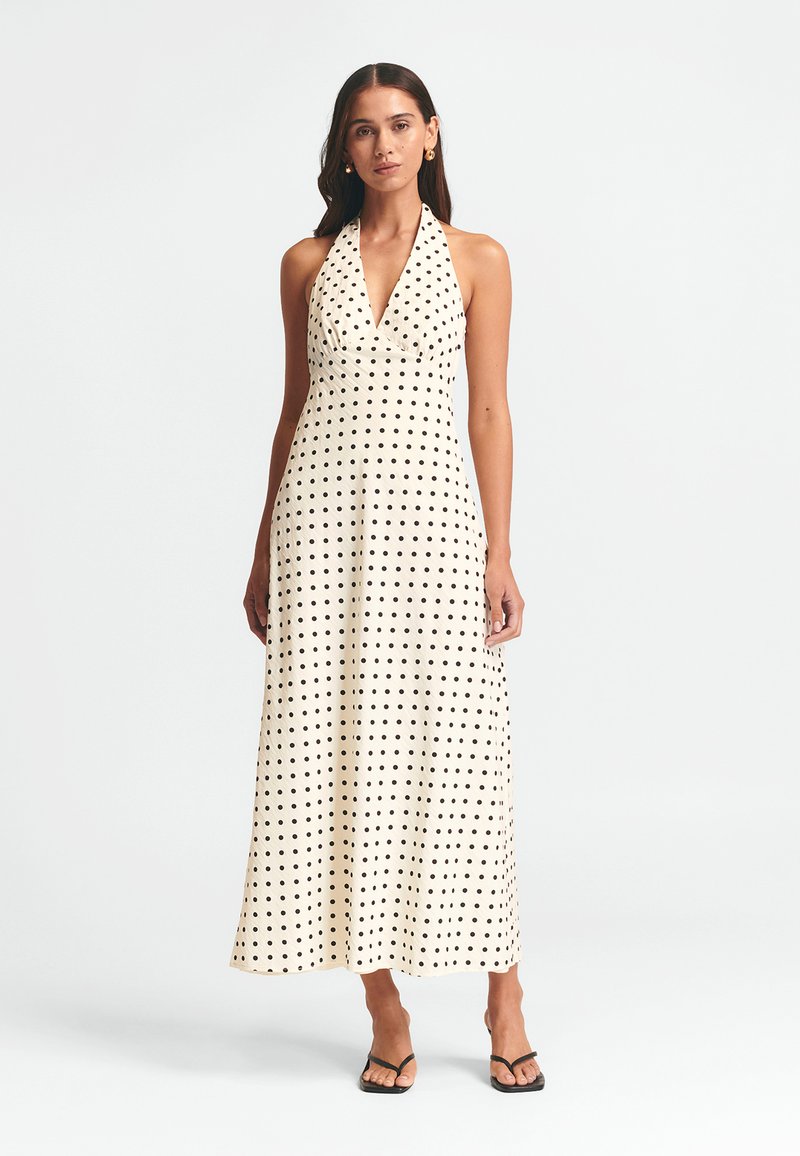 Vestido maxi de tirantes con estampado de lunares en crema con puntos negros, con escote en V y tejido fluido. Llevado con sandalias negras.