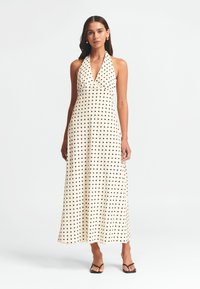 Kreemivärvi polka dot halter maxi kleit mustade täppidega, millel on V-kujuline kaelus ja voolav kangas. Kantud mustade sandaalidega.