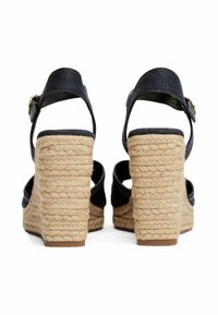 Black wedge sandals with a woven jute heel and ankle strap. Features textured fabric and a gold buckle accent.