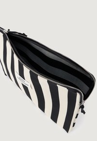 Καμβάς πούτσ με μαύρες και λευκές ρίγες, με κλείσιμο φερμουάρ, ευρύχωρο εσωτερικό με ριγέ σχέδιο. Το λογότυπο της μάρκας είναι ορατό στο μπροστινό μέρος.