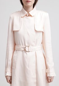 Jasnoróżowy płaszcz trencz z paskiem w talii, z klasycznym kołnierzem i guzikami. Gładka tkanina z ukrytymi kieszeniami i mankietami.