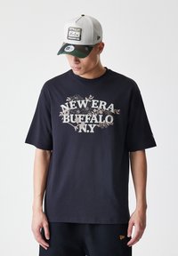 Črna bombažna majica s kratkimi rokavi, ki prikazuje grafiko "NEW ERA BUFFALO N.Y." v svetlo srebrni barvi, z ohlapnim krojem.
