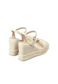 Sandali wedge beige con cinturini incrociati, dotati di una suola intermedia in juta intrecciata, una tomaia in faux leather liscia e una fibbia laterale per la regolazione.