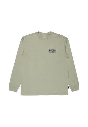 Camisa de cuello redondo de manga larga en un verde claro, con un pequeño gráfico rectangular en azul marino en el lado izquierdo del pecho que presenta texto y un logotipo de ola.