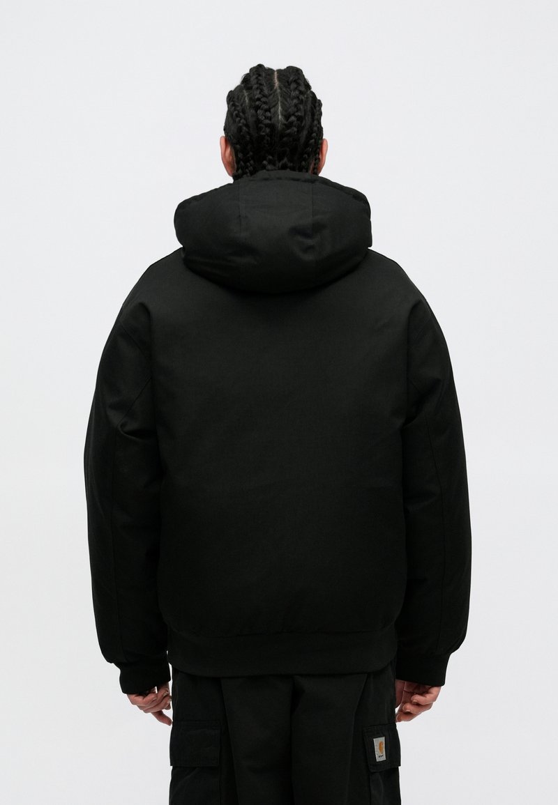 Chaqueta negra con capucha, de corte holgado, fabricada con un tejido texturizado. Presenta una gran capucha y puños acanalados en las muñecas y la cintura.