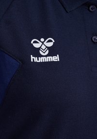 Marinblå pikétröja med texturerad väv, med en vit "hummel"-logotyp på bröstet och matchande mörka knappar.