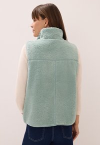 Fleeceväst i ljusmyntgrön med hög krage, strukturerad textil och sömdetaljer; använd över en ljus topp och parat med mörka jeans.