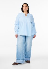 Blusa a righe blu chiaro e bianca con scollo rotondo e dettaglio con fiocco, abbinata a jeans in denim chiaro a gamba larga e scarpe con stampa leopardata.