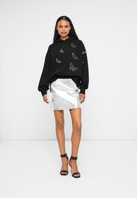Sudadera negra de gran tamaño con detalles de mariposa, combinada con una mini falda plateada metálica y sandalias negras de tacón alto.