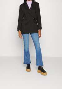 Svart dubbelknäppt blazer med bälte i midjan, i kombination med ljusblå utsvängda jeans och kraftiga svarta plattformsanklar.