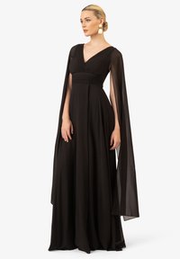 Abito da sera nero con scollatura a V, corpetto plissettato e maniche a mantella trasparenti. Il tessuto fluente crea una silhouette liscia e un drappeggio elegante.