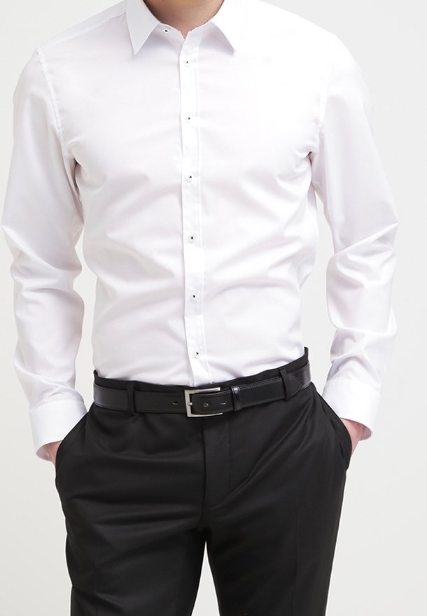 Camicia bianca con colletto classico e bottoni neri, abbinata a pantaloni eleganti neri e una cintura nera con fibbia metallica.