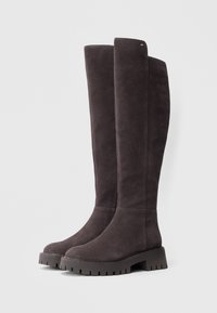 På kneet høy mørkegrå semskede støvler med tykke, teksturerte gummisåler og minimal søm. Har en liten gullaccent på siden.