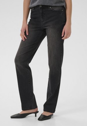 Person wearing black straight-leg jeans and black low-heel pointed mule shoes, standing against a plain light background.