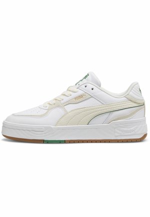 Biały niski sneaker Puma z beżowym paskiem z zamszu, zielonymi akcentami logo i gumową podeszwą na jednolitym białym tle.