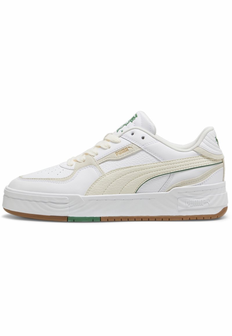 Baskets basses blanches Puma avec bande beige en suède, accents verts du logo et semelle en gomme sur fond blanc uni.