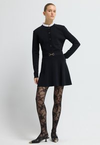 Černé šaty s dlouhými rukávy, zlatým zapínáním na knoflíky, kapsou a opaskem se zdobným zlatým akcentem. Nosit s vzorovanými černými punčochy a špičatými botami.