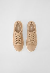 Light beige suede sneakers with rounded toes, flat laces, and a textured off-white rubber sole. Minimalist design and clean lines.