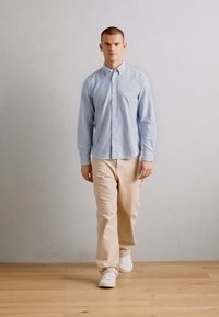 Lys blåstripet skjorte med knapper, beige bukser og hvite joggesko. Skjorten har krage og lange ermer. Enkel, uformell stil.