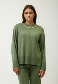 Groene gebreide trui met een hoge hals en een decoratieve kollektion van rhinestones; heeft een losse pasvorm en geribde manchetten, gecombineerd met bijpassende broek.