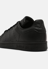 Sorte læder sneakers med perforerede detaljer, tekstureret sål og præget branding på hælen. Klassisk lavt design med glat finish.