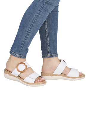 Sandales compensées blanches avec une semelle semblable à du liège et deux brides. Une bride est ornée d'un grand accent rond. Portées avec un jean bleu.